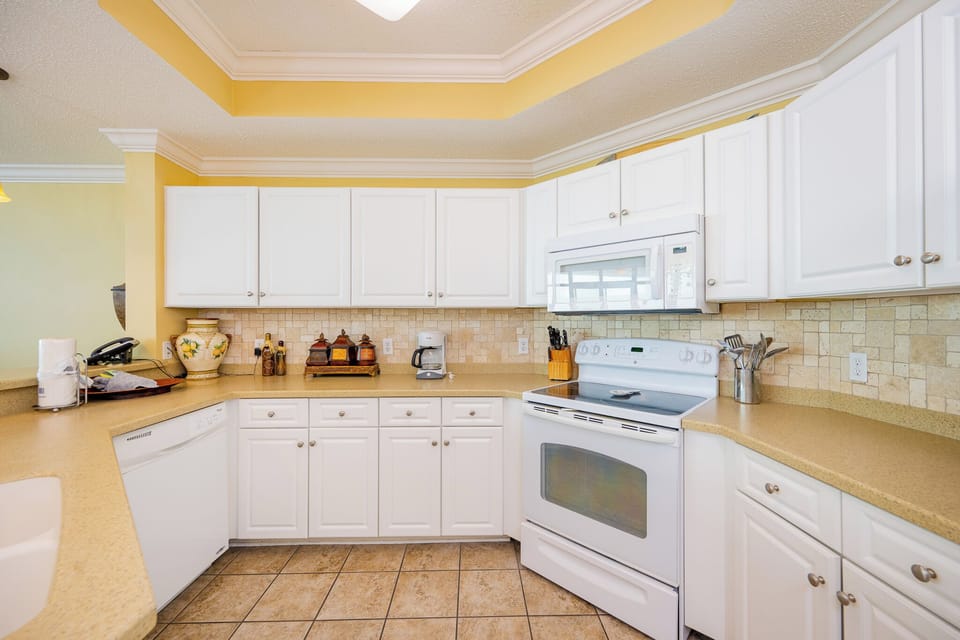 Prepare meals in this kitchen with sleek cabinetry, white appliances, and spacious countertops