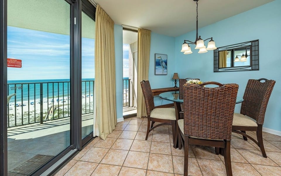 Natural light floods the dining area where you gather around a glass table with a view from the balcony