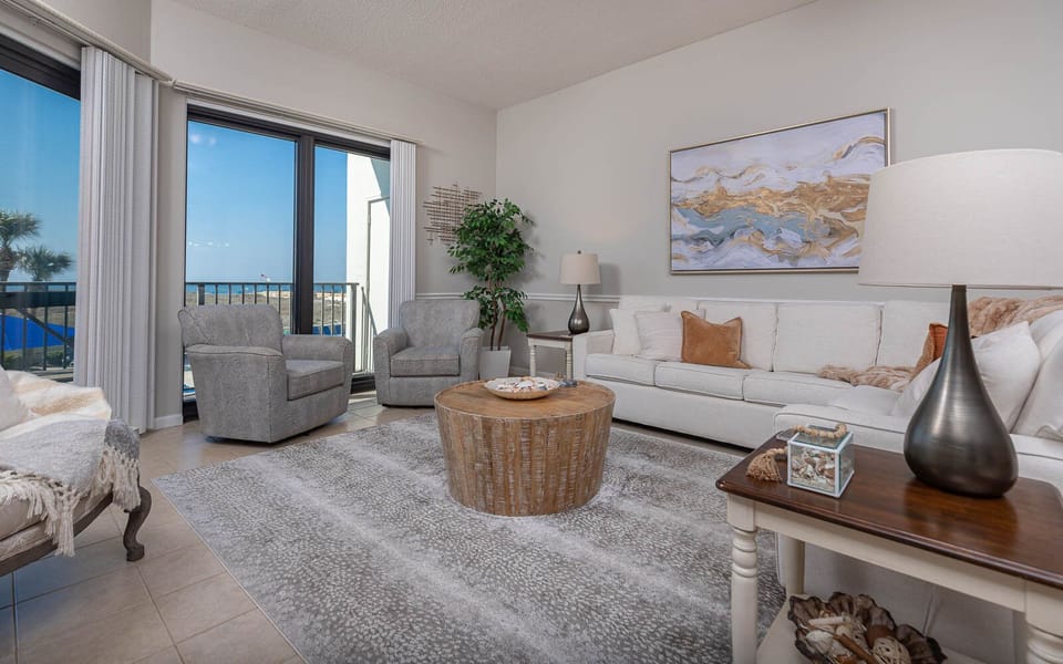 Bright living area featuring a cozy sofa with queen sleeper, accent chairs, and balcony with a view of the beach