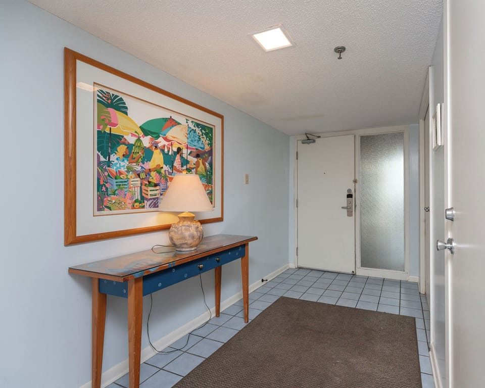 Colorful artwork adorns the wall above a wooden console table with a lamp, welcoming guests into the bright entryway