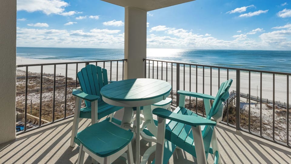 Turquoise chairs circle your balcony table where sunlight shimmers over the gulf coastline