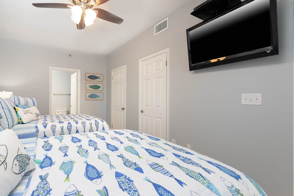 Rest in this guest bedroom featuring two cozy queen beds and a wall-mounted TV
