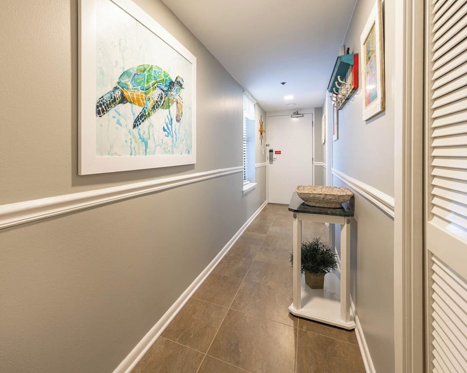 Step into a welcoming hallway adorned with beach art and natural light, leading you to your vacation retreat