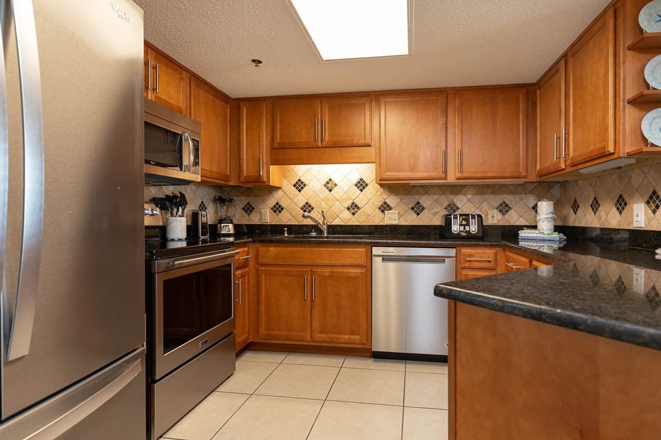 The kitchen features warm wood cabinetry, black countertops, and stainless appliances for a seamless cooking experience