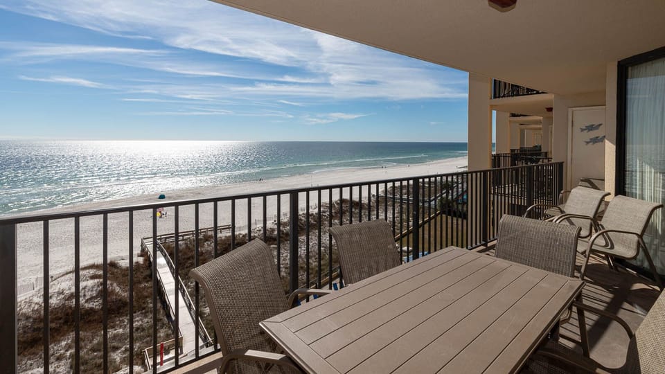 A spacious balcony features a dining table and chairs, offering a serene view of the beach and sparkling water beyond