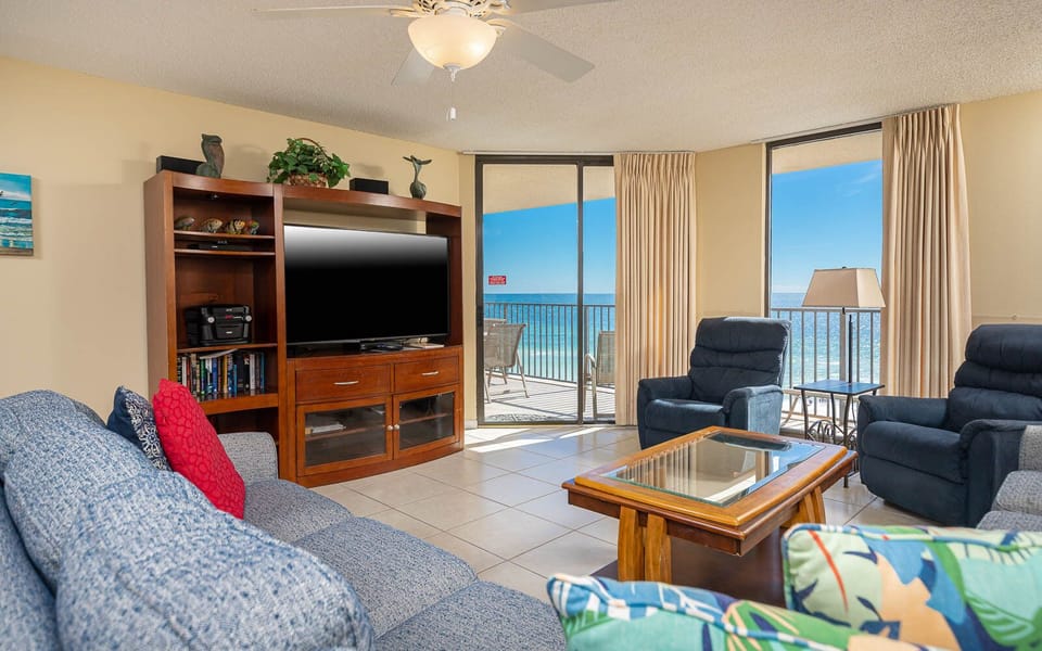 Living area features a cozy blue sofa with queen sleeper, two recliners, coffee table, and a stunning beach view