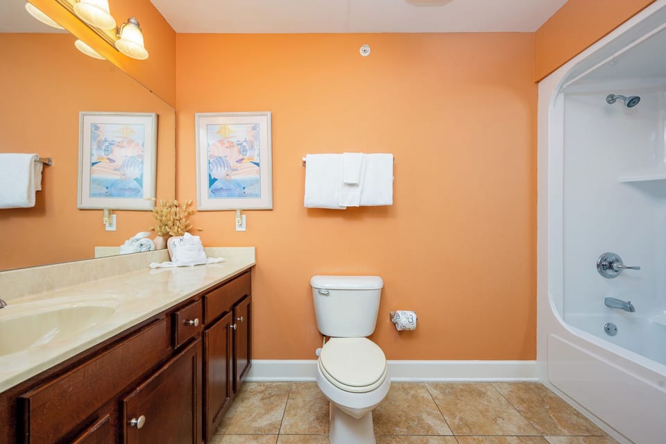 This bathroom features warm orange walls, a spacious vanity with a large mirror, and a relaxing tub for your comfort