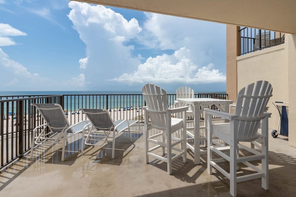 This spacious extended balcony features white outdoor furniture, perfect for enjoying the breathtaking beach view