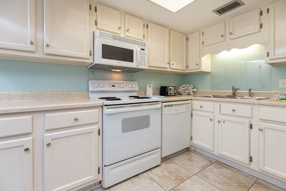 This kitchen features white cabinetry, stainless appliances, and a cheerful coastal color scheme, perfect for meal prep