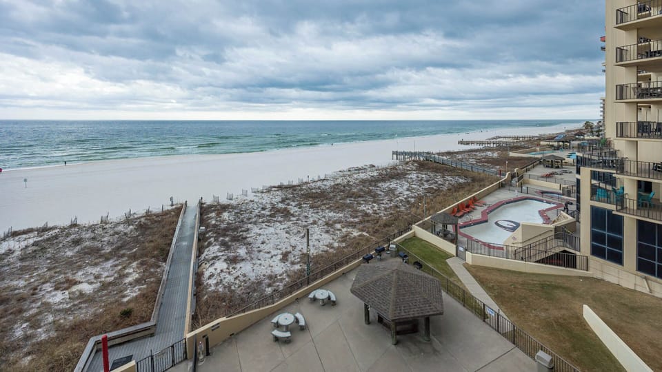 Expansive beachfront view showcasing white sand and gentle waves, with a nearby gazebo and seating area for relaxation