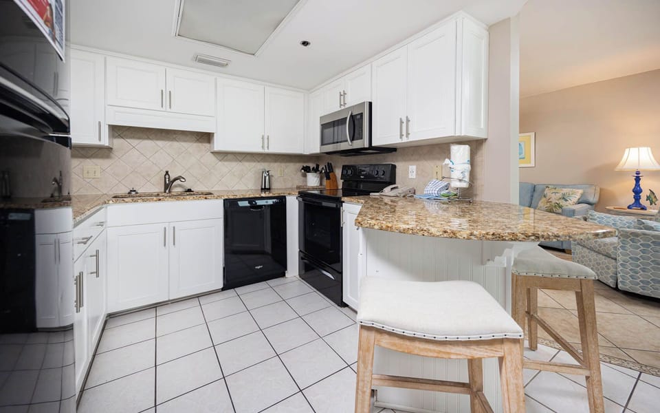 White cabinetry complements the granite countertops in this fully-equipped kitchen with a breakfast bar and seating