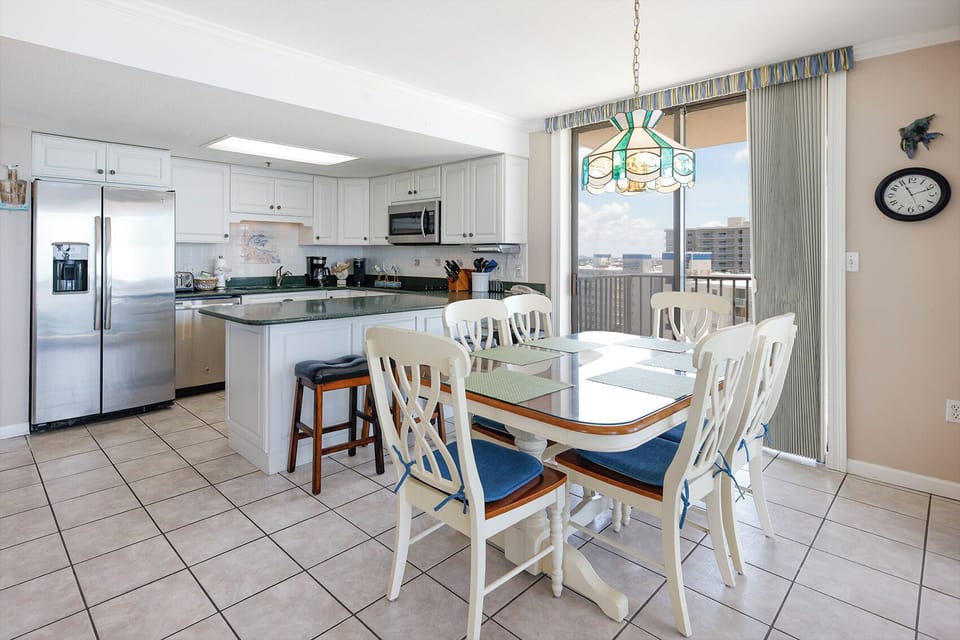 Bright kitchen area features white cabinetry, a breakfast bar with seating, and a dining table with blue-accented chairs