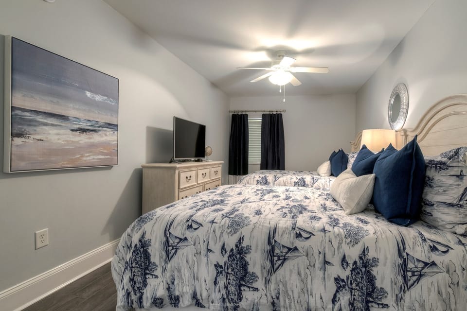 Spacious coastal bedroom with two queen beds, TV, and en-suite access

