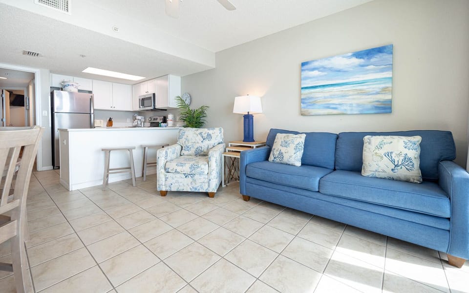 Relax in the comfortable living area, featuring a blue sofa, floral chair, and a view of the kitchen space beyond