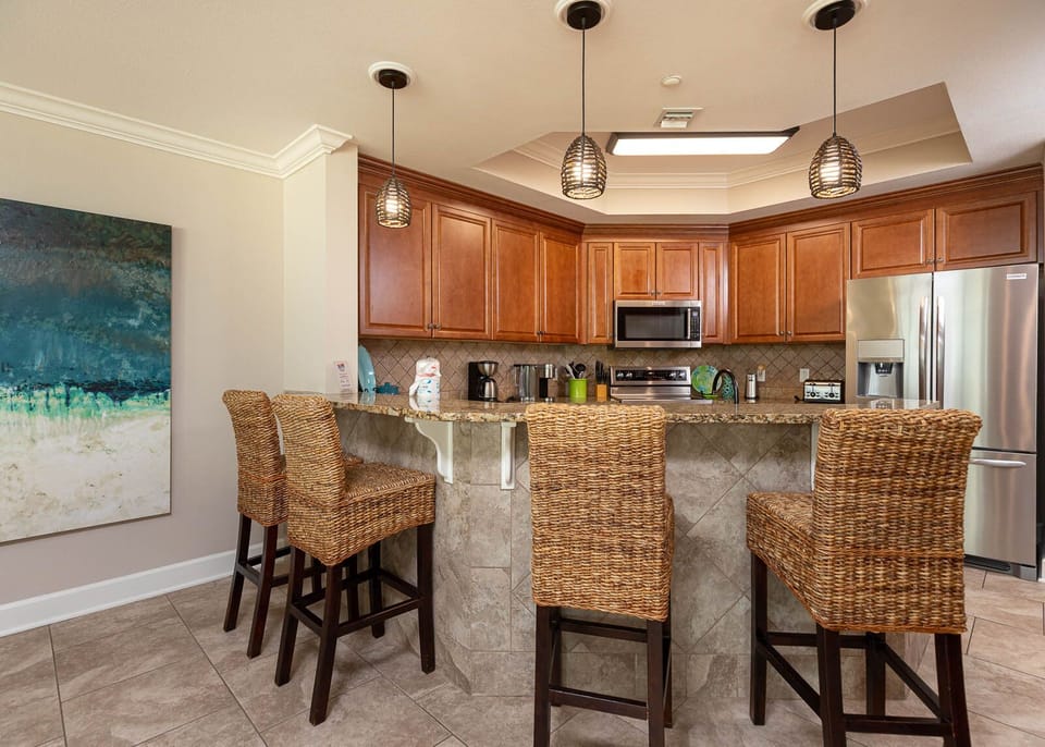This kitchen features warm wood cabinetry, granite countertops, stainless appliances, and a cozy bar area with woven stools