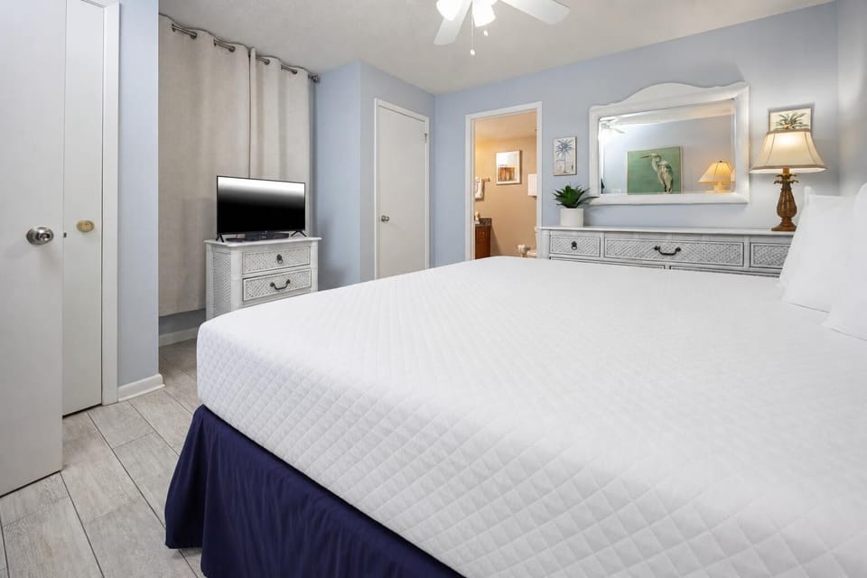 Bright guest bedroom featuring a large king bed, a TV on a decorative dresser, and a doorway leading to a bathroom
