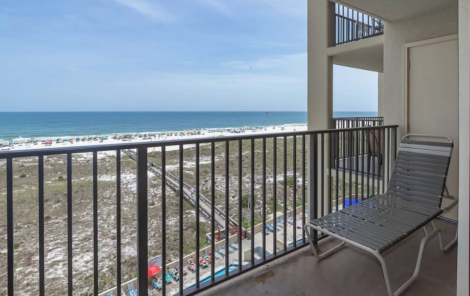 Balcony view showcasing the beach, with white sand and colorful umbrellas lining the shore, perfect for relaxation