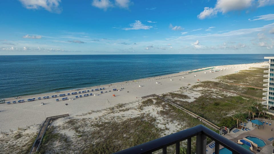Gaze at the tranquil waters and beach from your balcony, where colorful umbrellas dot the shore for your enjoyment