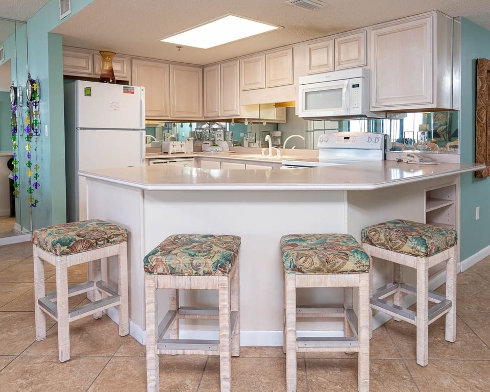 Kitchen area features light cabinetry, a breakfast bar with four cushioned stools, and modern appliances for convenience