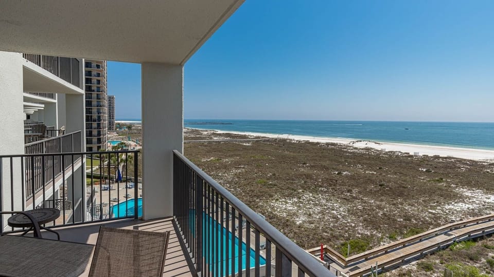 Balcony view showcasing the tranquil gulf, white sand beach, and the pool area surrounded by lush greenery