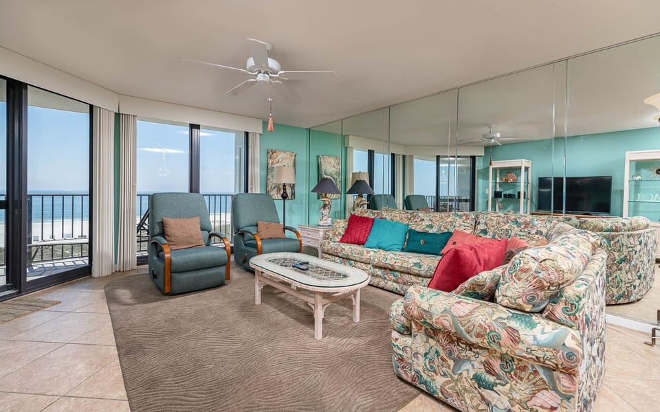 Living area features a floral-patterned sofa with queen sleeper, two armchairs, and a view of the beach