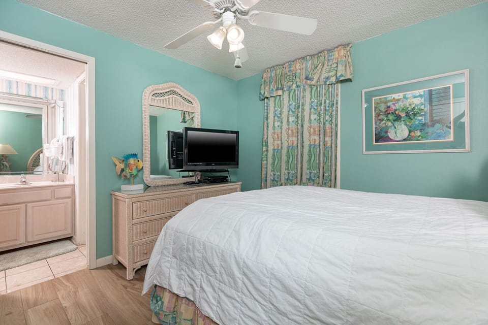 Turquoise walls complement a cozy guest bedroom featuring a queen bed, dresser, TV, and a view into the adjoining bathroom