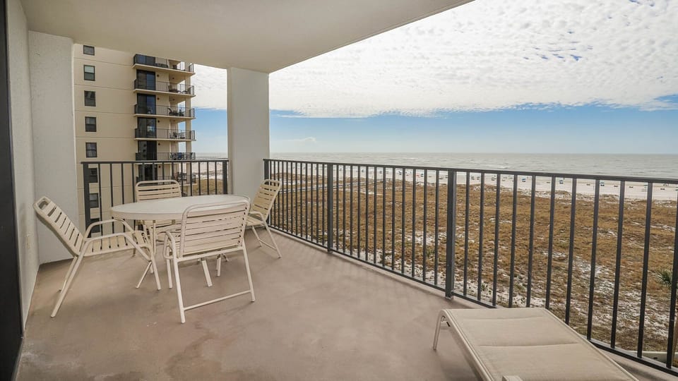 Balcony with a table and chairs offers a view of the beach and gulf, perfect for enjoying the coastal breeze