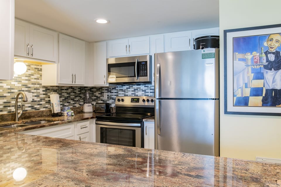 Kitchen with solid wood cabinets, granite tops, tiled backsplash, Keurig K cup & drip style coffee maker, stainless steel appliances including range, above range microwave, pots, pans, blender