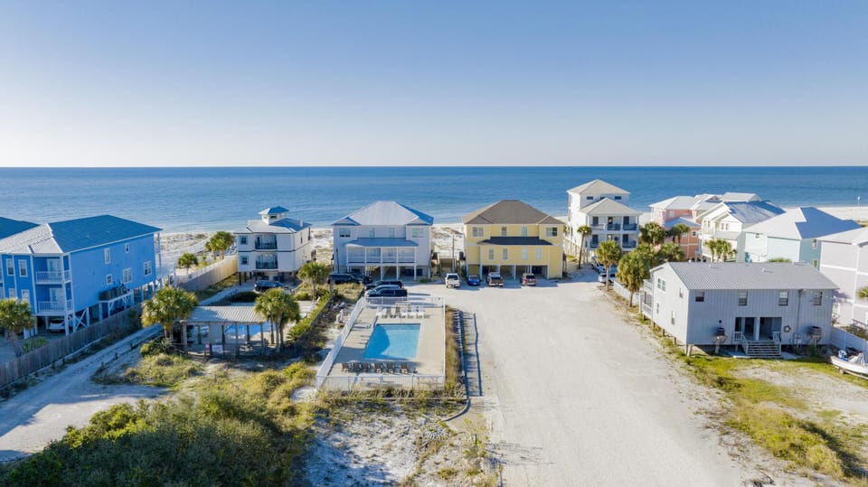 Aerial view of the fenced rectangular pool surrounded by lounge chairs and palm trees, with the Gulf shoreline in the background.