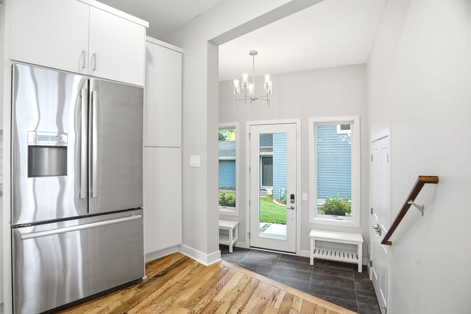 Step into this bright, modern space where your vacation begins. Gleaming stainless steel appliances and crisp white cabinetry welcome you home, while natural light pours through the glass-paneled entry door framing views of the landscaped surroundings.