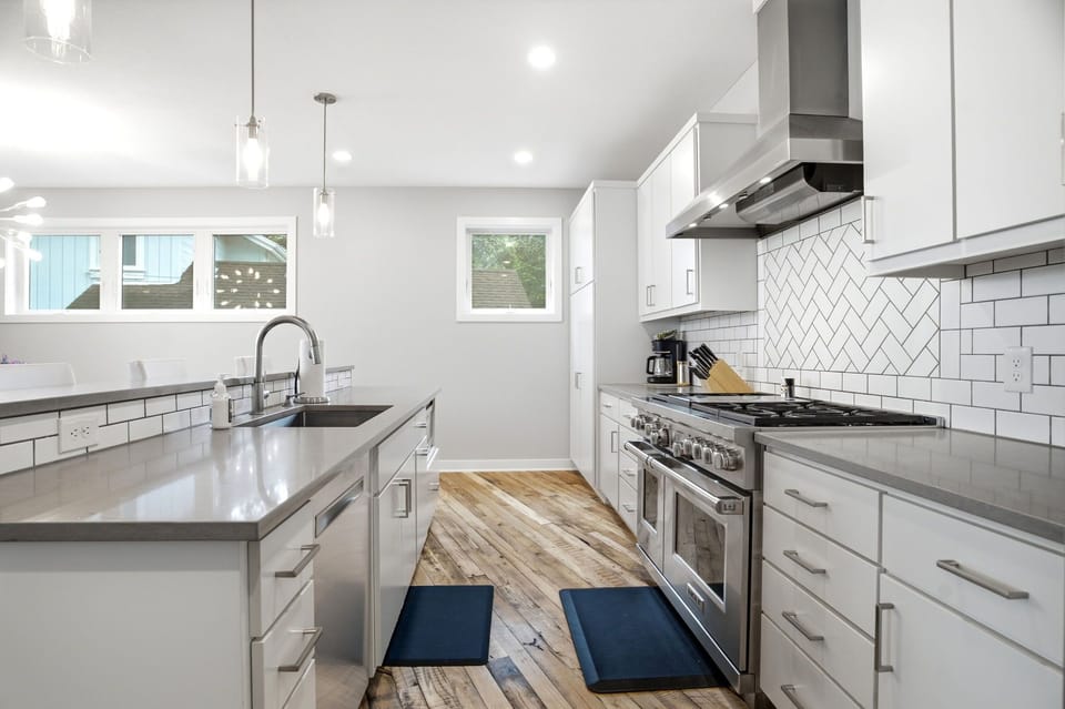 Your fully equipped modern kitchen features sleek white cabinetry, quartz countertops, stainless appliances, and a herringbone tile backsplash—perfect for preparing delicious home-cooked meals during your stay.