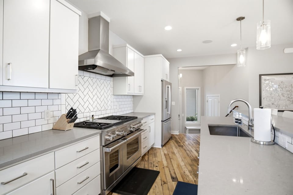 A bright modern kitchen awaits, with sleek white cabinetry, stainless steel appliances, and elegant herringbone tile backsplash. You'll love preparing meals in this stylish, fully-equipped space with ample counter room and contemporary finishes.