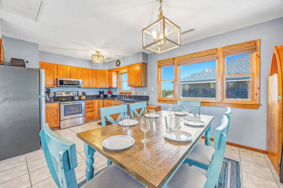 This cheerful kitchen and dining area welcomes you with warm wood cabinetry, modern appliances, and a farmhouse table set for memorable meals together under charming pendant lighting.