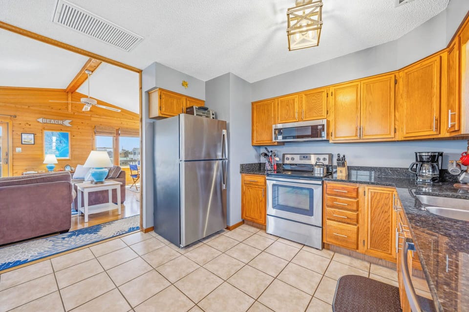 Your fully equipped kitchen features modern appliances and ample counter space for preparing meals, with warm wood cabinetry and tile flooring opening to the sunny living area.