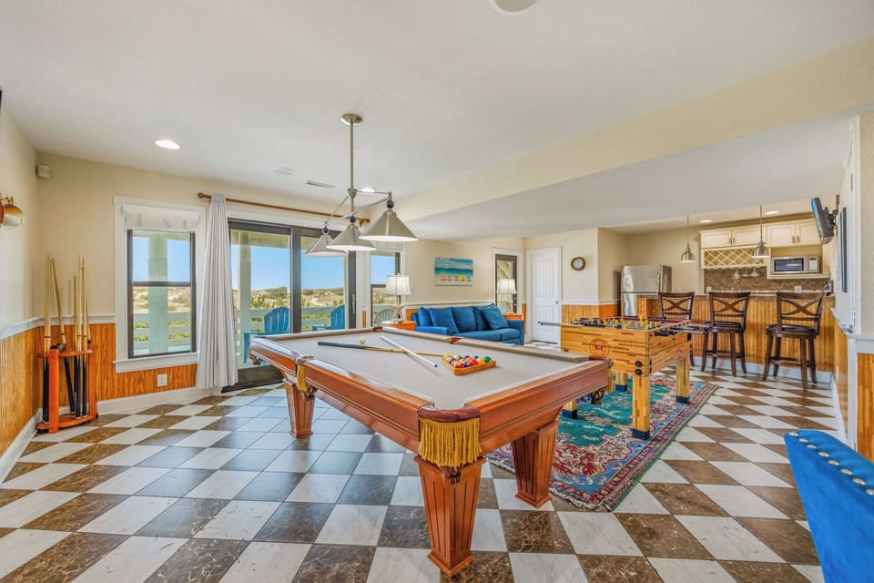 Step into an entertainer's dream space where friendly competition awaits at the pool table, panoramic water views frame every shot, and the open kitchen invites you to gather with loved ones over meals and games.