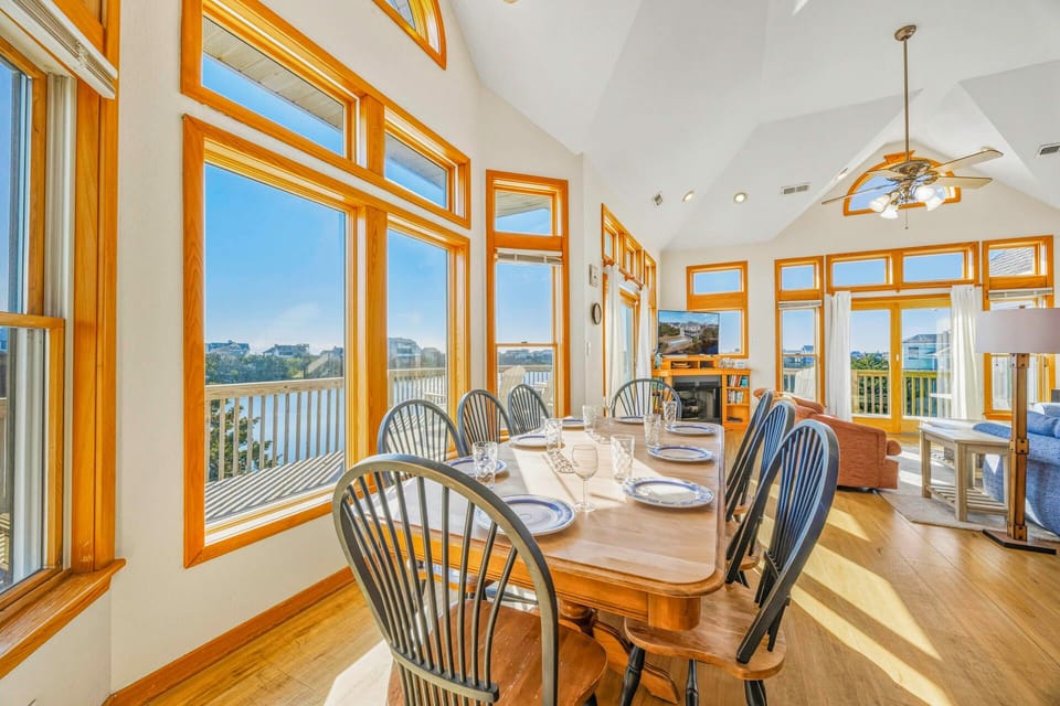 Gather around this sun-drenched dining table where warm wood tones and soaring windows create your perfect space for memorable meals together.