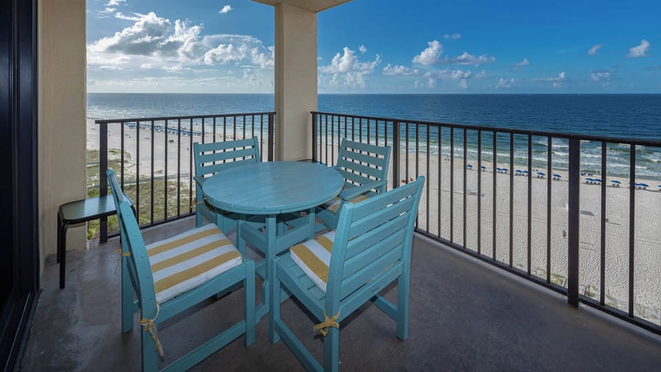 A turquoise table set with striped cushions offers a relaxing spot to enjoy the beachfront view from the balcony