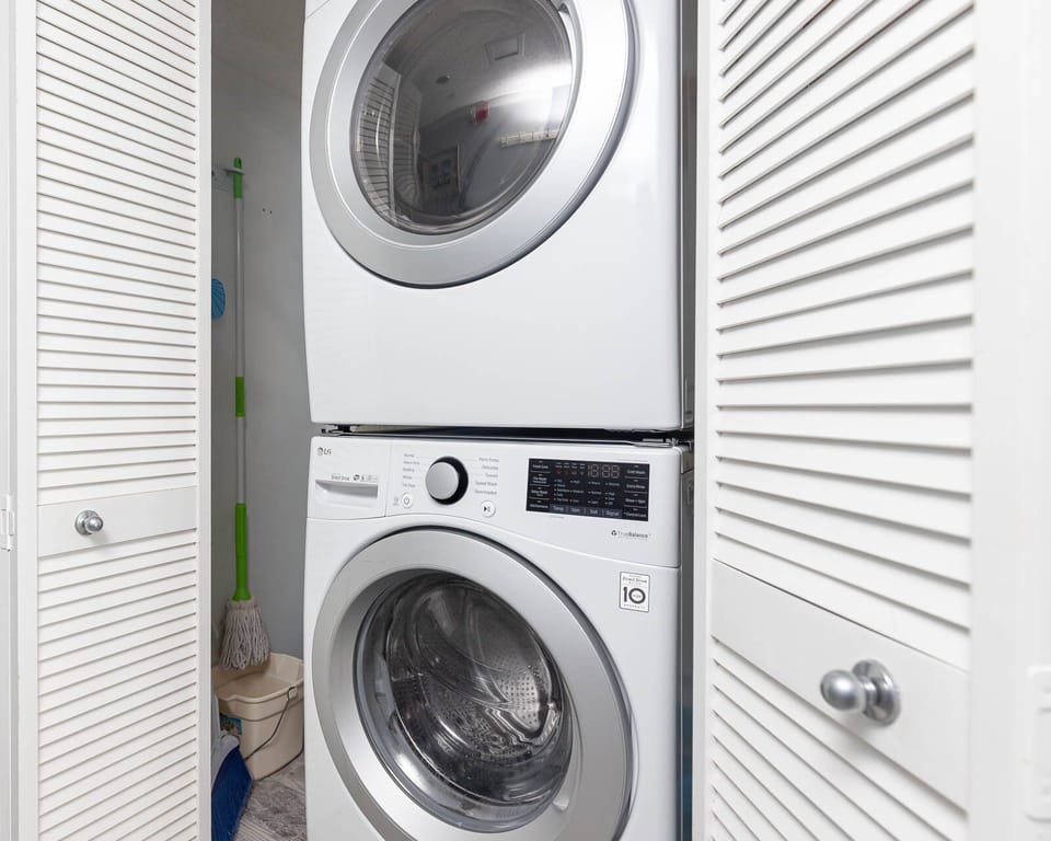 Stacked washer and dryer in a compact laundry area with white cabinetry and cleaning supplies neatly stored beside them