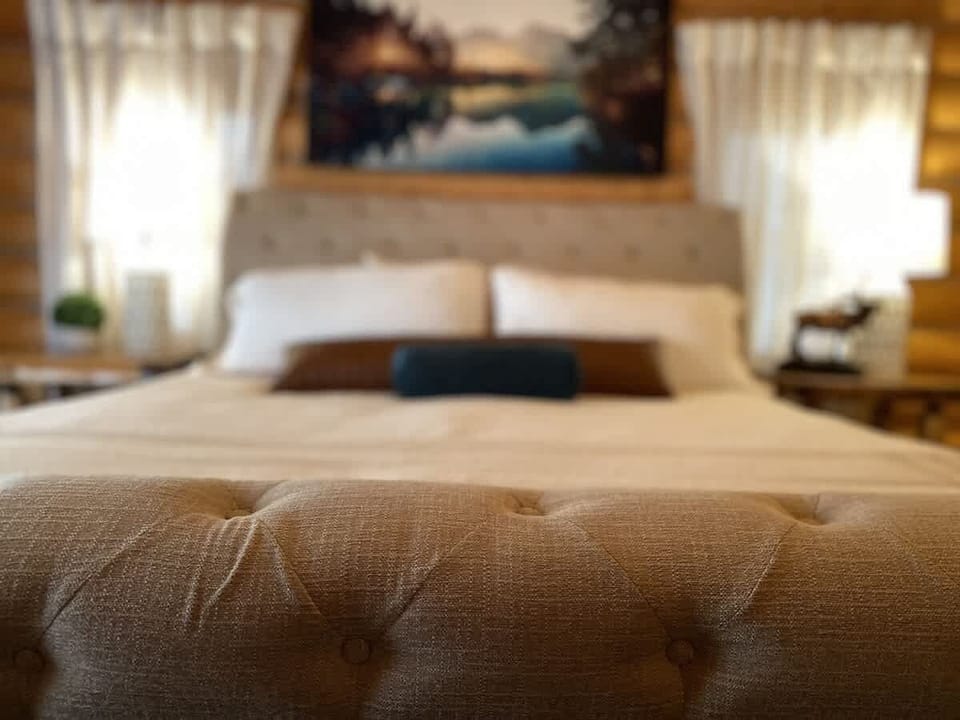 A large king-sized bed with a duvet is positioned at the center of the room, flanked by matching nightstands with stylish lamps that emit a soft, warm glow.