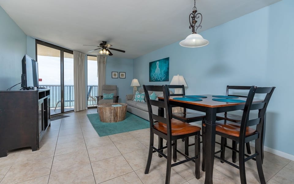 The living area features a cozy sofa with queen sleeper, dining table, and large windows offering a view of the beach front