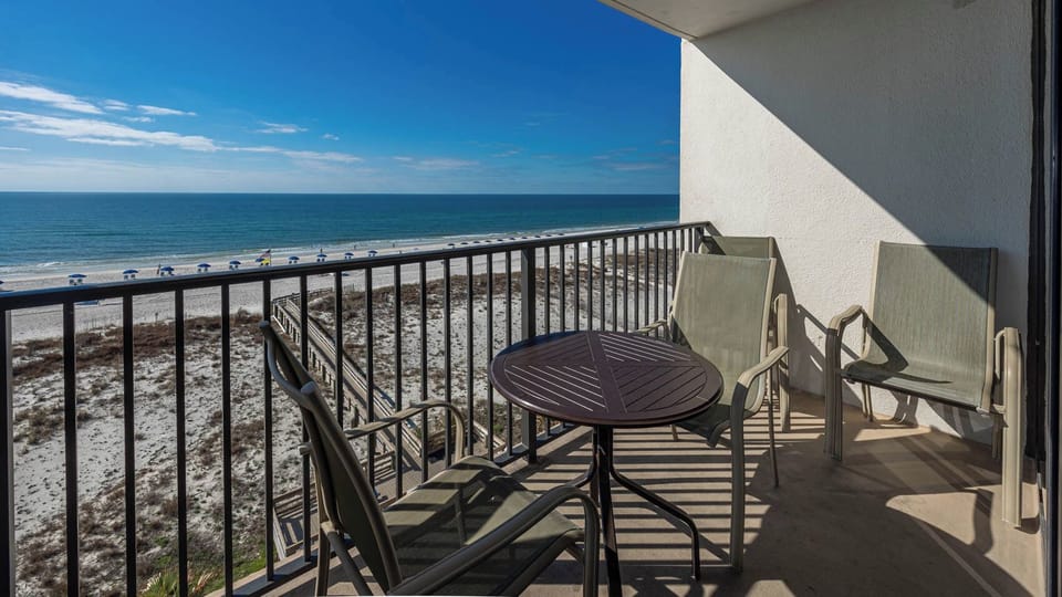 Enjoy a relaxing view from the balcony with a table and chairs overlooking the beach and sparkling waters