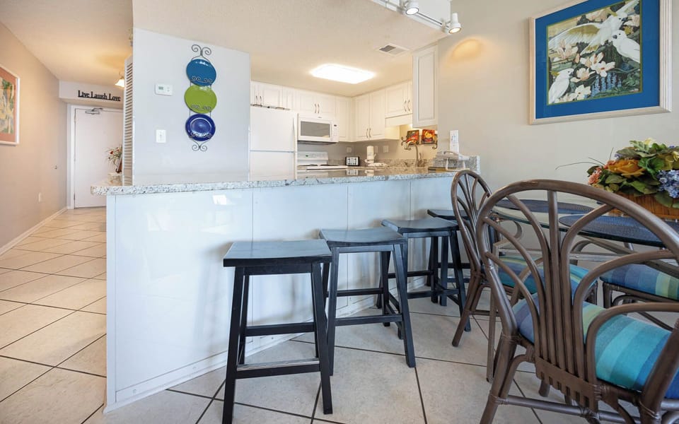 This kitchen features sleek white cabinetry, a granite countertop, and a cozy dining area with colorful seating