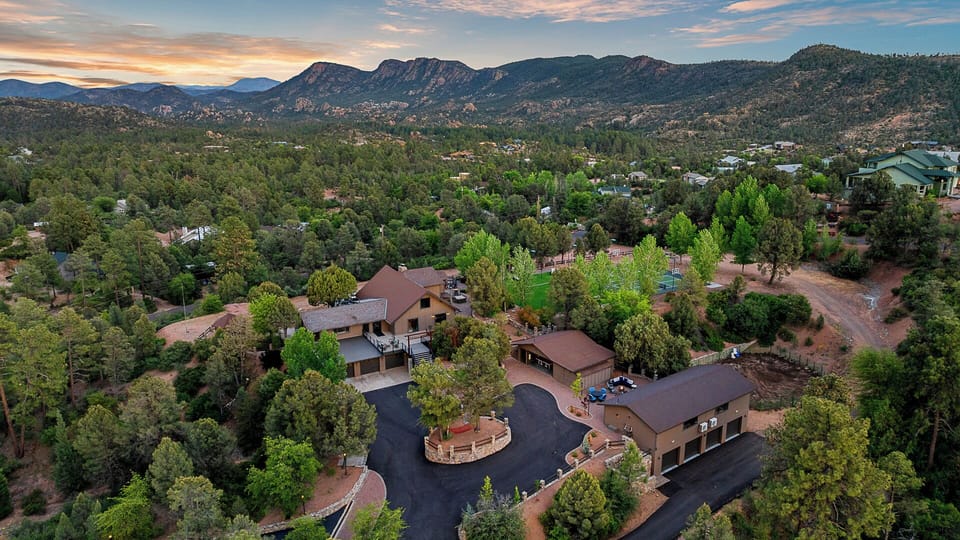 Secluded mountain estate with multiple buildings, lush forest, and sunset views.