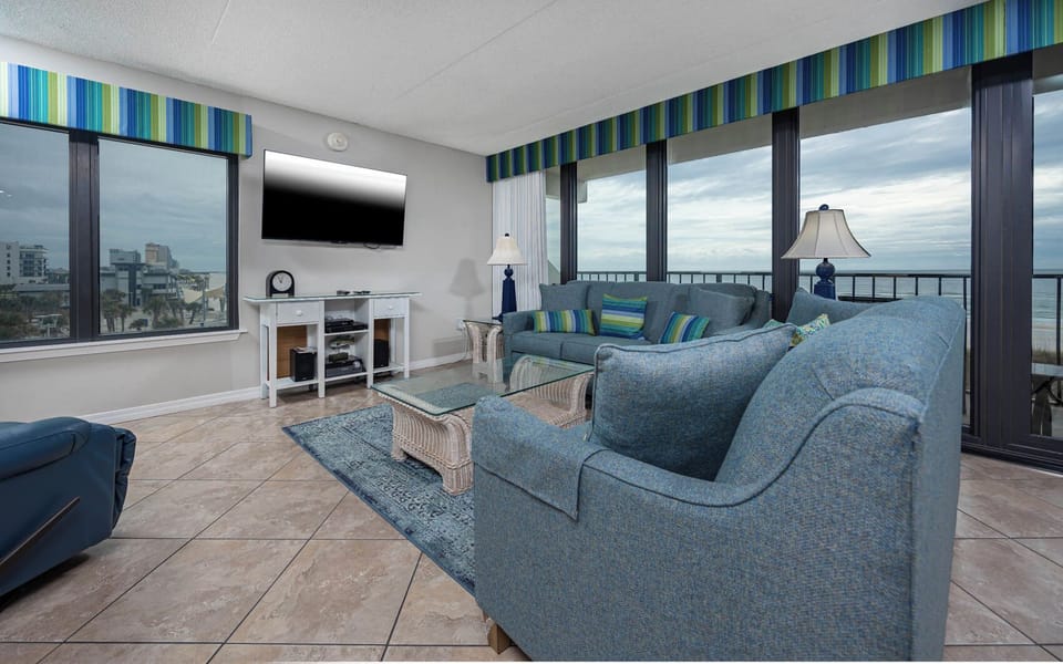 The living area features a comfortable couch and stunning views of the beachfront through large windows