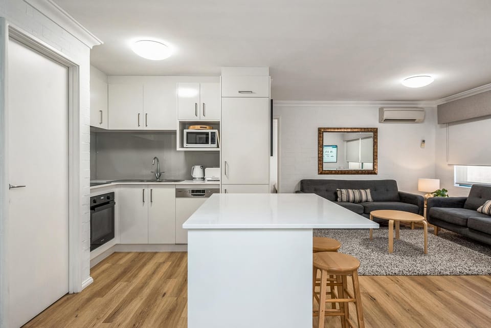 White quartz island with three wooden stools separates the kitchen and living area with gray sofas and a round coffee table.