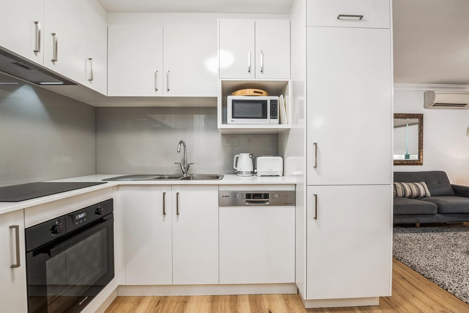 Compact kitchen with white cabinetry, stainless steel appliances, and a gray glass backsplash above the sink.