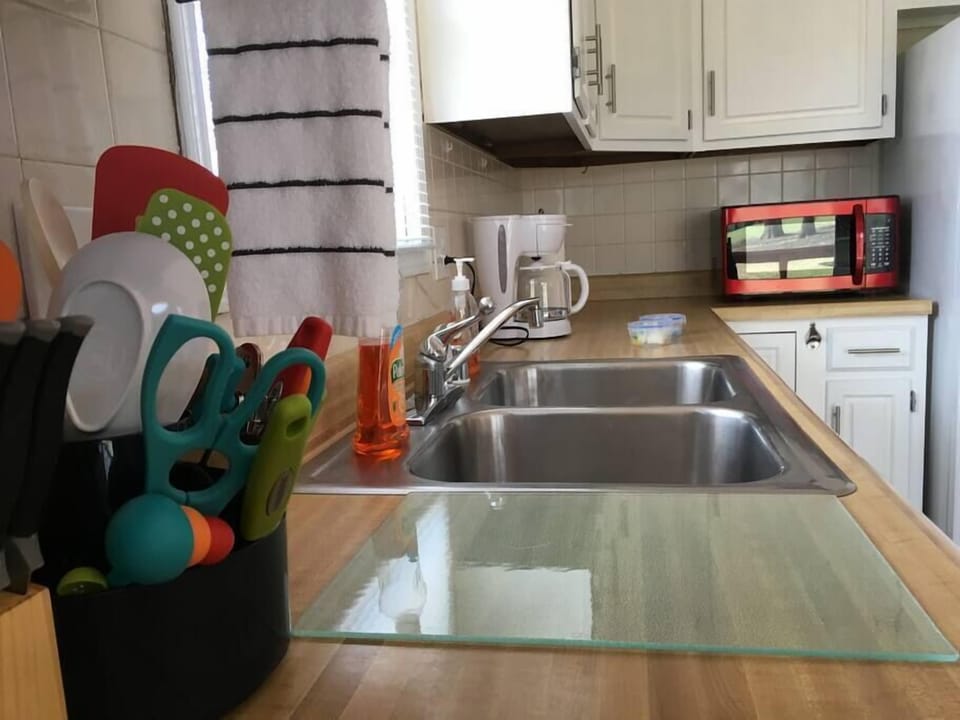 Double stainless steel sink set in wood countertops with white cabinetry and red microwave in kitchen.