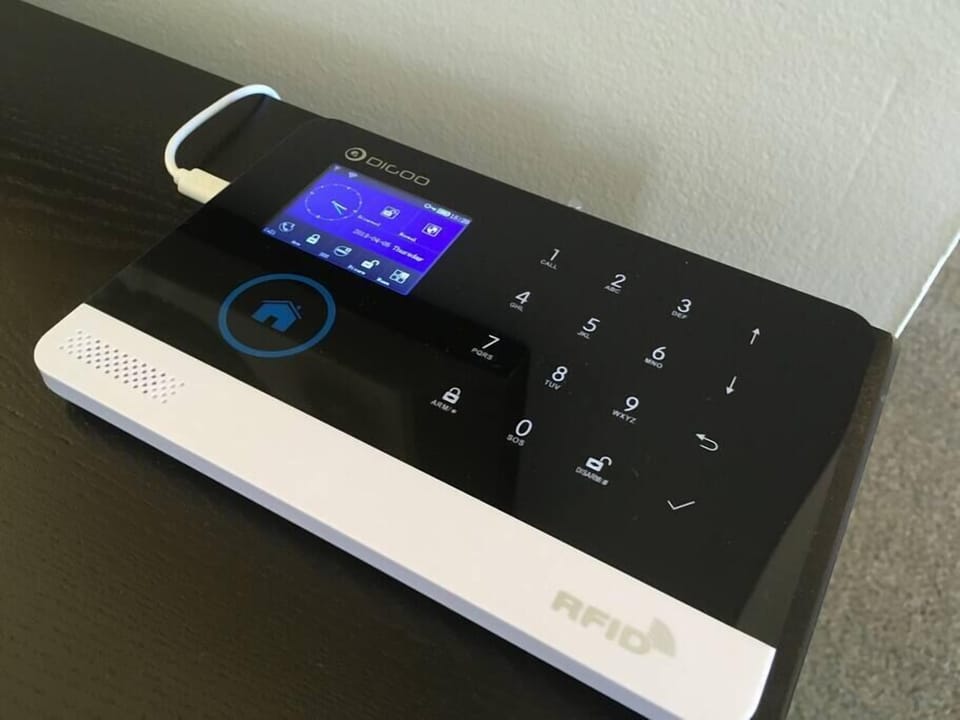 Security alarm panel with touchscreen display and numeric keypad on a dark wood surface.