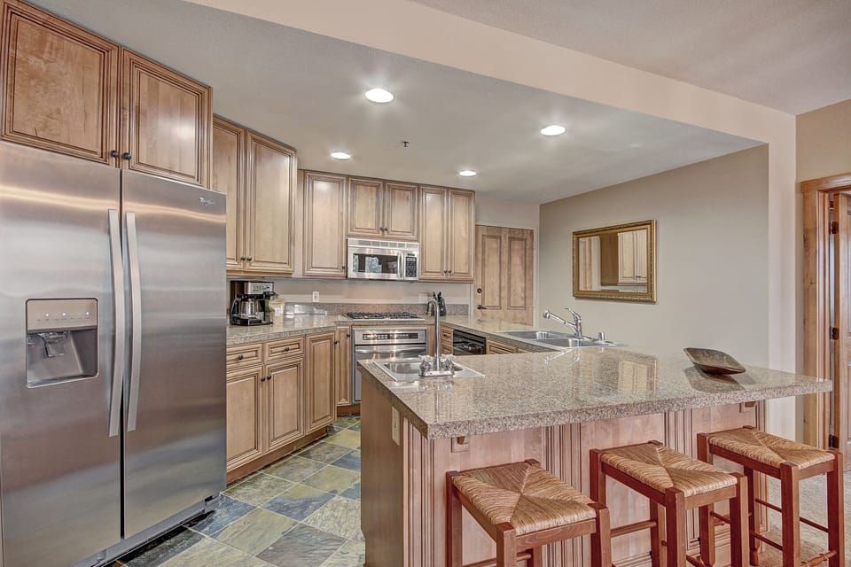 Modern kitchen with stainless steel appliances, wood cabinets, granite countertops, an island with bar seating, and tiled floor.