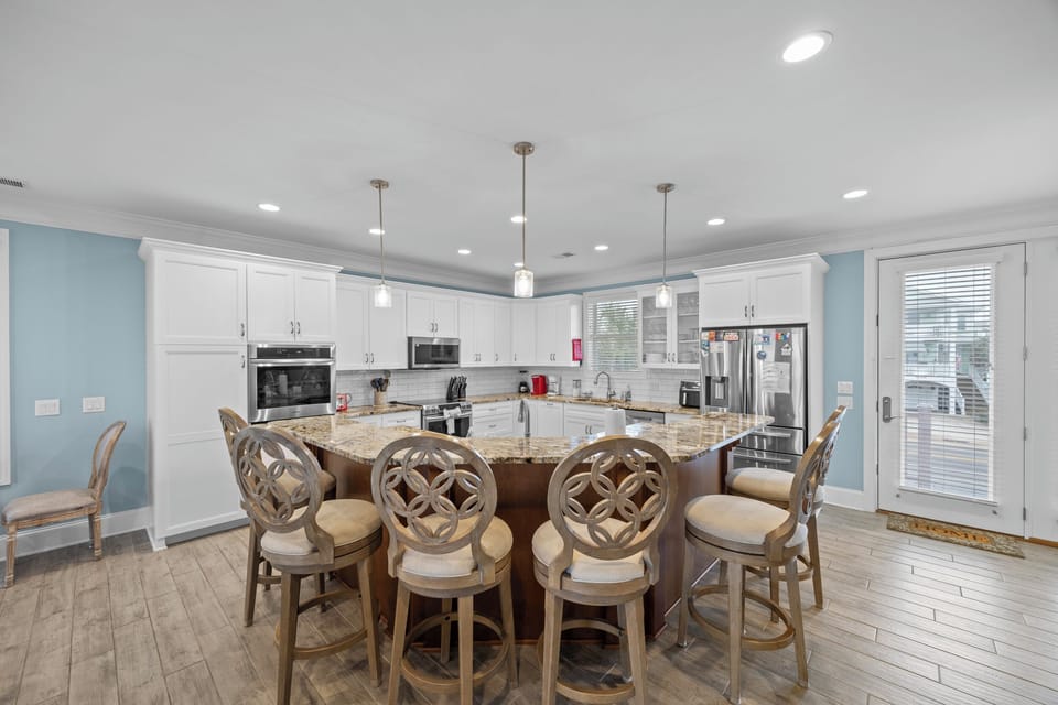 Your elegant kitchen features granite island seating, stainless appliances, and gorgeous white cabinetry bathed in natural light.